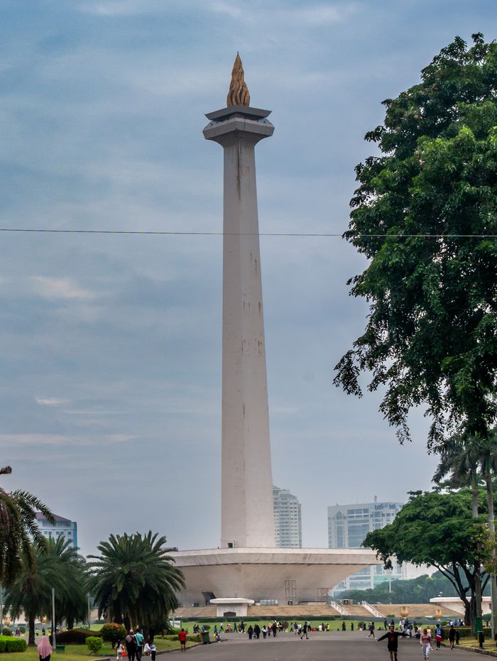 Services View of Jakarta's iconic National Monument surrounded by greenery under a cloudy sky.